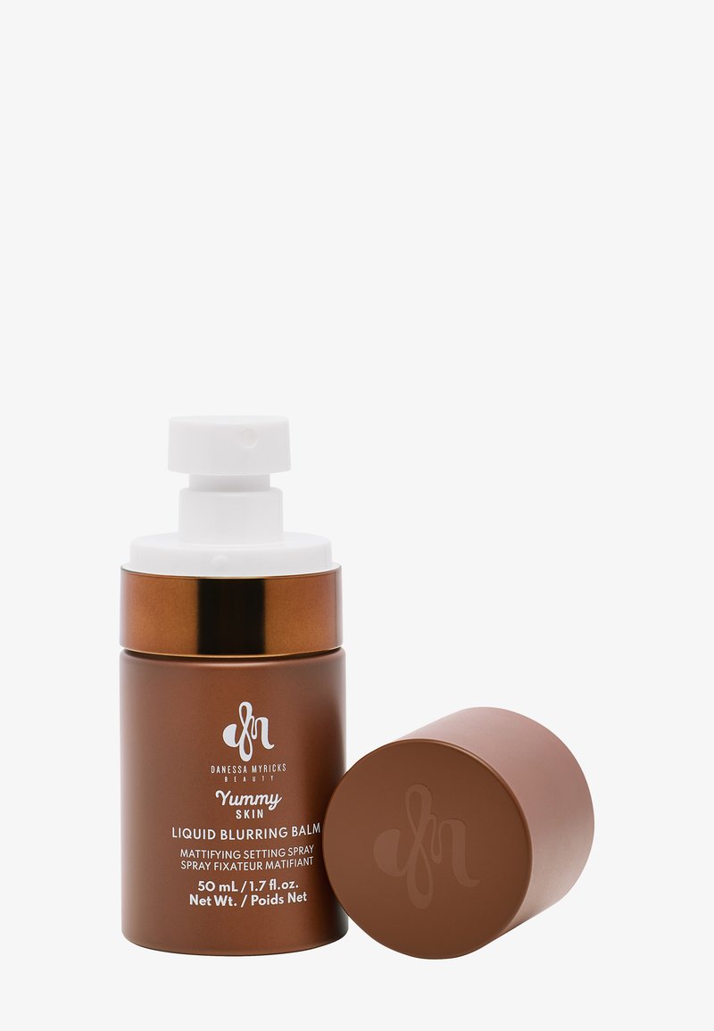 Brun glassflaske med hvit pumpe dispenser, merket "Yummy Skin Liquid Blurring Balm," inneholder 50 mL av produktet, matte finish.