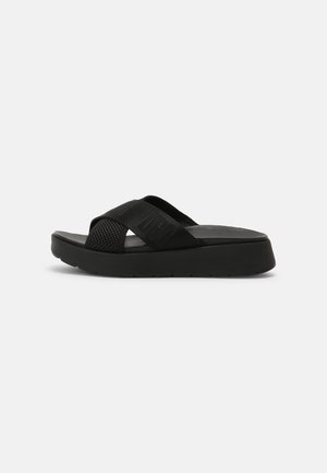 Sort slip-in sandal med krydsede stropper i tekstureret stof og en solid platformsål med let forhøjelse.