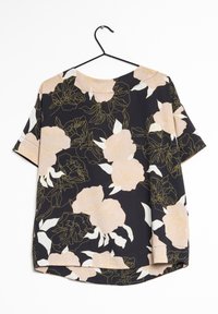 Blusa nera a maniche corte con un motivo floreale in pesca chiaro e bianco, caratterizzata da dettagli dorati e una vestibilità rilassata. Appesa a un gancio nero.