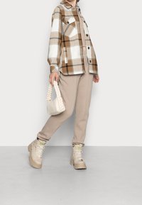Plaid button-up shirt in brown and white, beige sweatpants, beige combat boots, and a small braided handbag.
