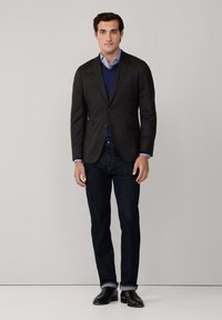 Blazer nero sopra un maglione blu navy e una camicia azzurra, abbinato a jeans scuri e scarpe nere. Tessuto morbido con dettagli di taglio su misura.
