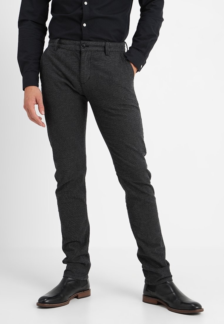 Dark gray tailored pants featuring a textured fabric, slim fit design, and front pockets. Worn with a black button-up shirt and black boots.