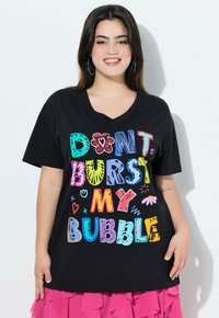 T-shirt in cotone nero con scollo a V, caratterizzato da un testo colorato e giocoso "NON FAR SCOPPIARE LA MIA BOLLA" in vari font e dettagli grafici.