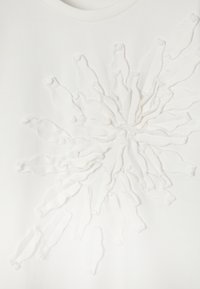 Material alb cu un model floral texturat și reliefat, realizat din benzi moi buclate care radiază din centru.