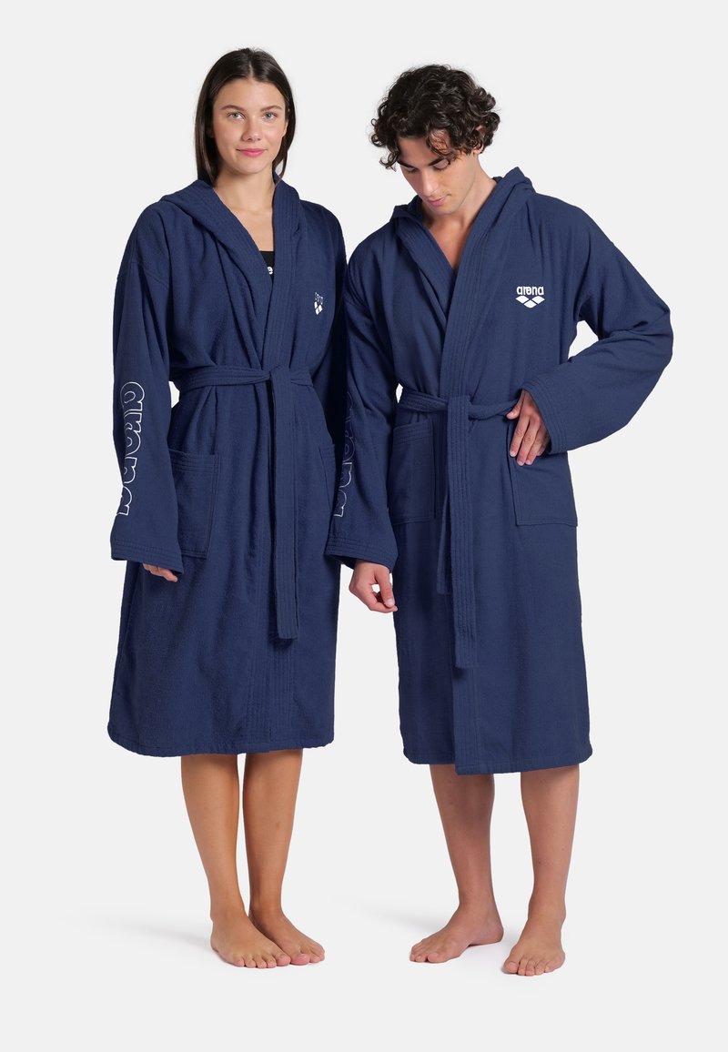 Accappatoi in cotone blu navy con cappuccio e cintura, dotati di due tasche frontali e dettagli con logo sulle maniche. Tessuto leggero e testurizzato.