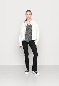 Casaco branco oversized sobre uma blusa escura com estampado floral, combinado com calças pretas justas e ténis preto e branco. Design simples, visual casual.