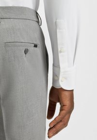 Pantalons en lin gris avec une texture subtile, dotés d'une poche arrière boutonnée et d'une chemise blanche à manches rehaussées d'une texture.