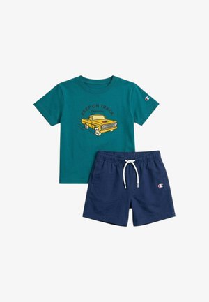 Maglietta a maniche corte verde petrolio con camion giallo e scritta "Keep on Track" abbinata a pantaloncini blu navy con laccio bianco, entrambi con logo Champion.