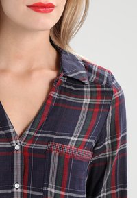Geruit overhemd met knopen in een marineblauw, rood en groen patroon. Heeft een kraag, borstzak en een lichte textuur.