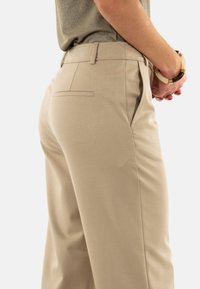 Pantaloni beige su misura con tasche laterali, una tasca posteriore e una vestibilità slim. Realizzati in un tessuto morbido con una leggera lucentezza.