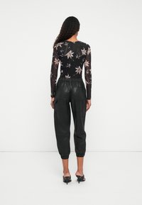Top negro de manga larga con un patrón floral, combinado con pantalones cargo de piel negra de cintura alta y puños elásticos. Diseño minimalista.