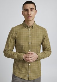 OLIVEDRAB-rutede skjorte med knap-ned krave, lange ærmer og hvide knapper. Har et subtilt logo på brystlommen.