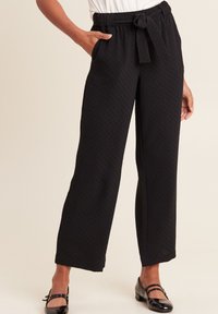 Pantaloni neri a gamba larga realizzati in tessuto texturizzato, con una vita elastica e cintura con la possibilità di essere legata, e tasche laterali.