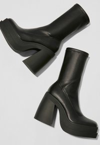 Botines negros de tobillo hechos de suave cuero sintético. Presentan tacones gruesos y una suela plataforma, con un diseño elegante y sin costuras.