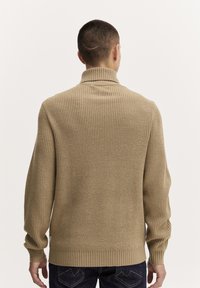 Beige, neulotut neulepusero, jossa on korkea kaulus sekä ribbiresorit hihansuissa ja helmassa. Takaa katsottuna neulepusero on väljä ja siinä on tekstuuriompelukuosi.