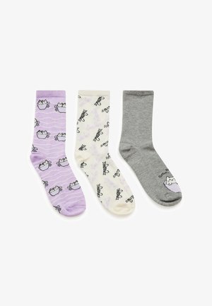 Trzy pary skarpetek: lawendowe z wzorem kotów i filiżanek, kremowe z konturami kotów oraz szare z wzorem kota. Różne kolory i nadruki.