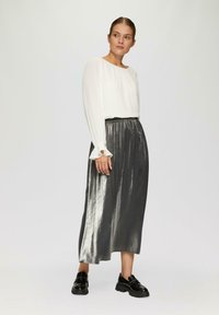 Witte plooibloes met uitlopende mouwen, gecombineerd met een glanzende, enkel-lange zilveren rok. Stevige zwarte schoenen maken de outfit compleet.