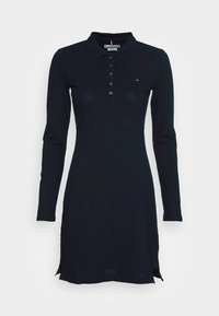 Marineblauwe polo jurk met lange mouwen, voorzien van een kraag, knoopsluiting, zijsplitten en een klein logo-accent op de borst. Soepele, rekbare stof.