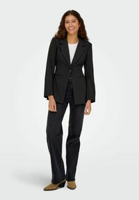 Mustriline mustriga bleiser, millel on üks nupp, nogelised kraed ja laiendatud varrukad, koos tumedate teksade ja beežide säärekingadega.