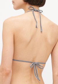 Svart og hvit gingham bikini topp med halterknuter. Har lukking med bakre knytning og en glatt tekstur. Enkel og funksjonell design.