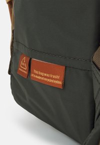 Sac en nylon vert à surface texturée, avec une étiquette marron indiquant "Ce sac était une poubelle ! Il est fabriqué en nylon recyclé."
