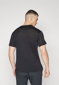 Camiseta negra de manga corta con cuello redondo, que presenta una textura sutil y aberturas laterales para facilitar el movimiento.