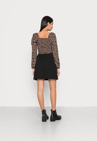 Saia preta combinada com uma blusa de manga longa castanha que apresenta um padrão floral preto. A blusa tem um decote quadrado e mangas bufantes. Botas pretas até o tornozelo.