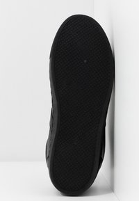 Semelle de chaussure noire avec une surface texturée et à motifs, comportant un point rond et la taille "38" en relief. Côté visible, montrant un design élégant.