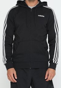 Sudadera con cremallera negra de mezcla de algodón, que presenta acentos de tres rayas blancas en las mangas, bolsillos delanteros y capucha con cordones.