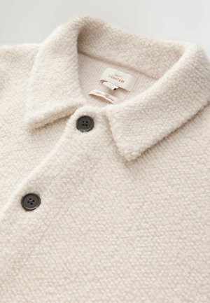 Kerman fleece-takki, jossa on kauluksellinen kaula-aukko, kaksi mustaa nappia ja pehmeä, teksturoidun pinnan. Merkitty "NEXT SIGNATURE."
