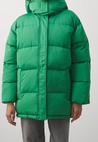 Grüne Pufferjacke mit hohem Kragen, Reißverschluss und kontrastierenden horizontalen Nähten. Verfügt über Fronttaschen und eine glatte, glänzende Textur.