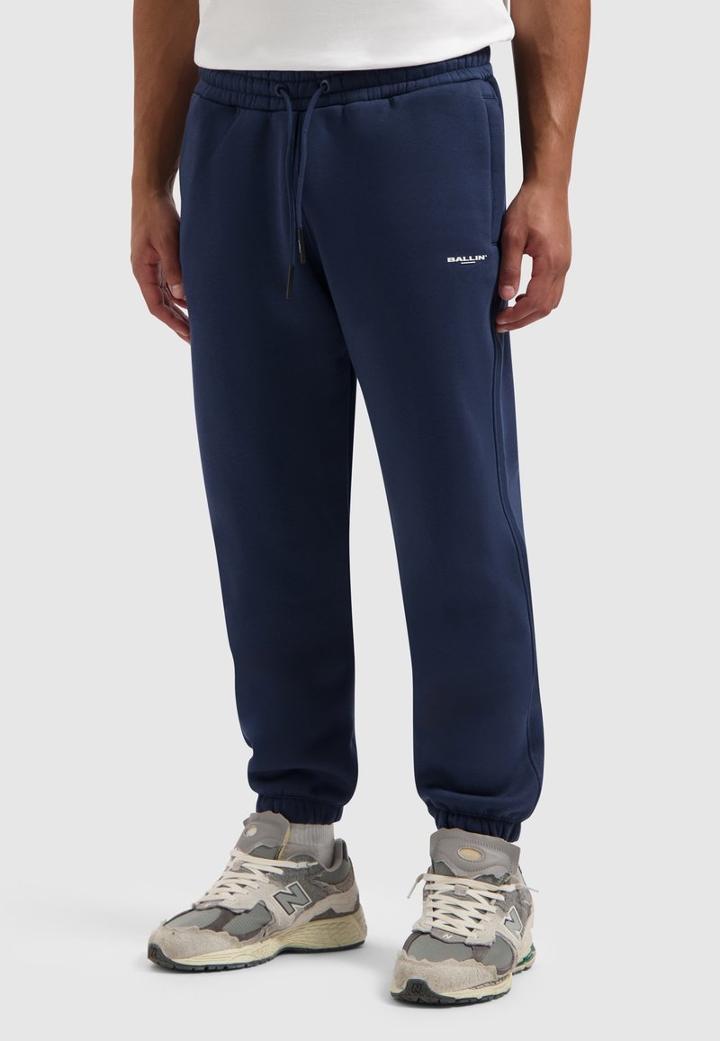Donkerblauwe sweatpants met een trekkoord in de taille, taps toelopende boorden en een katoenmix; heeft een wit logo op de linker bovenbeen.