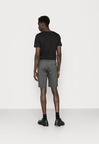 Zwarte t-shirt gecombineerd met grijze shorts met een elastische tailleband, slim fit en achtertas, gedragen met zwarte schoenen en sokken.