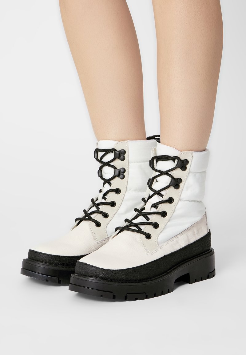 White and black lace-up boots featuring leather and padded textile upper, chunky black sole, with black laces and hardware accents.