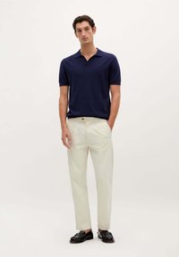 Mørkeblå polo shirt med kort krave, parret med cremefarvede, slim-fit bukser. Sorte loafers fuldender outfittet.