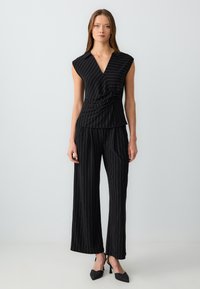 Completo a righe nere con top avvolgente a maniche corte e pantaloni palazzo. Il tessuto ha una superficie liscia con dettagli dorati.