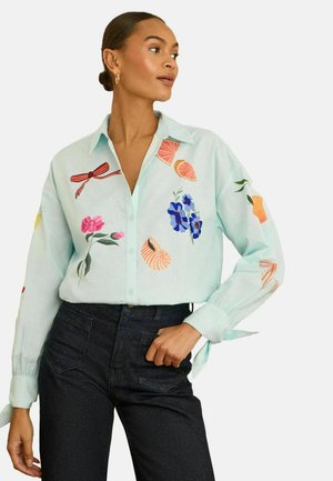 Svetlomodrá košeľa na zapínanie s rôznymi vyšívanými kvetinovými a ovocnými motívmi v žiarivých farbách. Má dlhé rukávy a voľný strih.