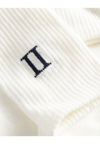 Tejido blanco acanalado con un detalle bordado en azul marino "II", que presenta una textura suave y un diseño limpio sin patrones ni accesorios.