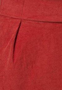 Tejido de pana en rojo oxidado con acanalado vertical. Presenta un detalle de plisado para mayor textura. Adecuado para ropa casual.