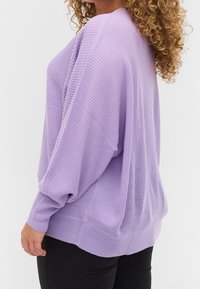 Lila gestrickter Pullover mit gerippter Textur, lockerer Passform und subtilen, abfallenden Schultern. Lange Ärmel und ein gerader Saum runden das Design ab.