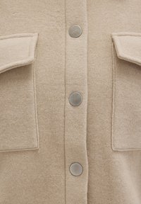Beige wool shirt featuring a button-down front, two chest pockets, metallic snap buttons, and a soft, textured finish.