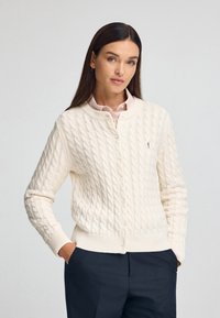 Cremfarbener Strickcardigan mit Rundhalsausschnitt, Knopfverschluss und gerippten Bündchen und Saum. Mit kleinem Logo auf der Brust.