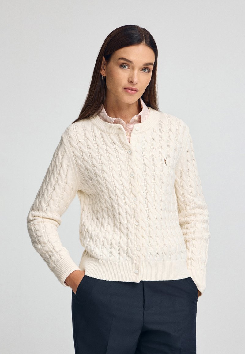 Cremfarbener Strickcardigan mit Rundhalsausschnitt, Knopfverschluss und gerippten Bündchen und Saum. Mit kleinem Logo auf der Brust.