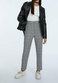 Zwarte leren motorjack, witte getailleerde top, grijs geruite high-waisted broeken en dikke witte loafers met gouden accenten.