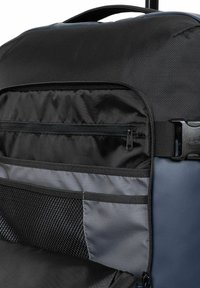 Mochila negra de nailon con bolsillos con cremallera, detalles de malla y una asa lateral. Presenta un acabado texturizado y correas ajustables.