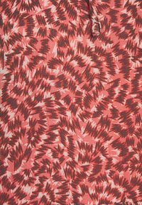 Gros plan d’un tissu avec des motifs en zigzag irréguliers marron foncé et beige sur fond rose corail, montrant les détails texturés et les coutures.