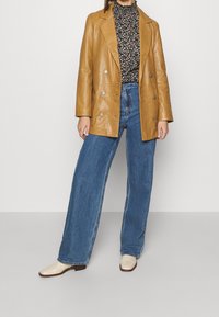 Bruine leren dubbelgeknoopte blazer, florale zwarte high-neck top, hoge taille blauwe wijde jeans en crèmekleurige enkelboots.