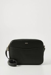 Čierna kožená taška cez rameno s hladkou textúrou, zaoblenými hranami a zipsovým uzáverom. Má logo a nastaviteľný popruh.