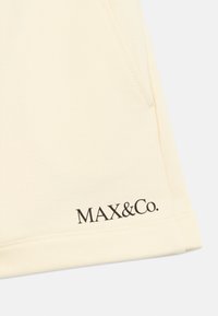 Απαλά, ανοιχτό κίτρινα υφασμάτινα σορτς με πλαϊνές τσέπες και μαύρο λογότυπο "MAX&Co." στη βάση. Λείο υλικό, προσαρμοσμένη σχεδίαση.