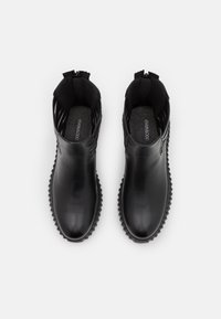 Czarne botki za kostkę z gładką skórzaną cholewką, teksturowaną podeszwą i unikalnym wycięciem w okolicy kostki, z zamkniętym noskiem.